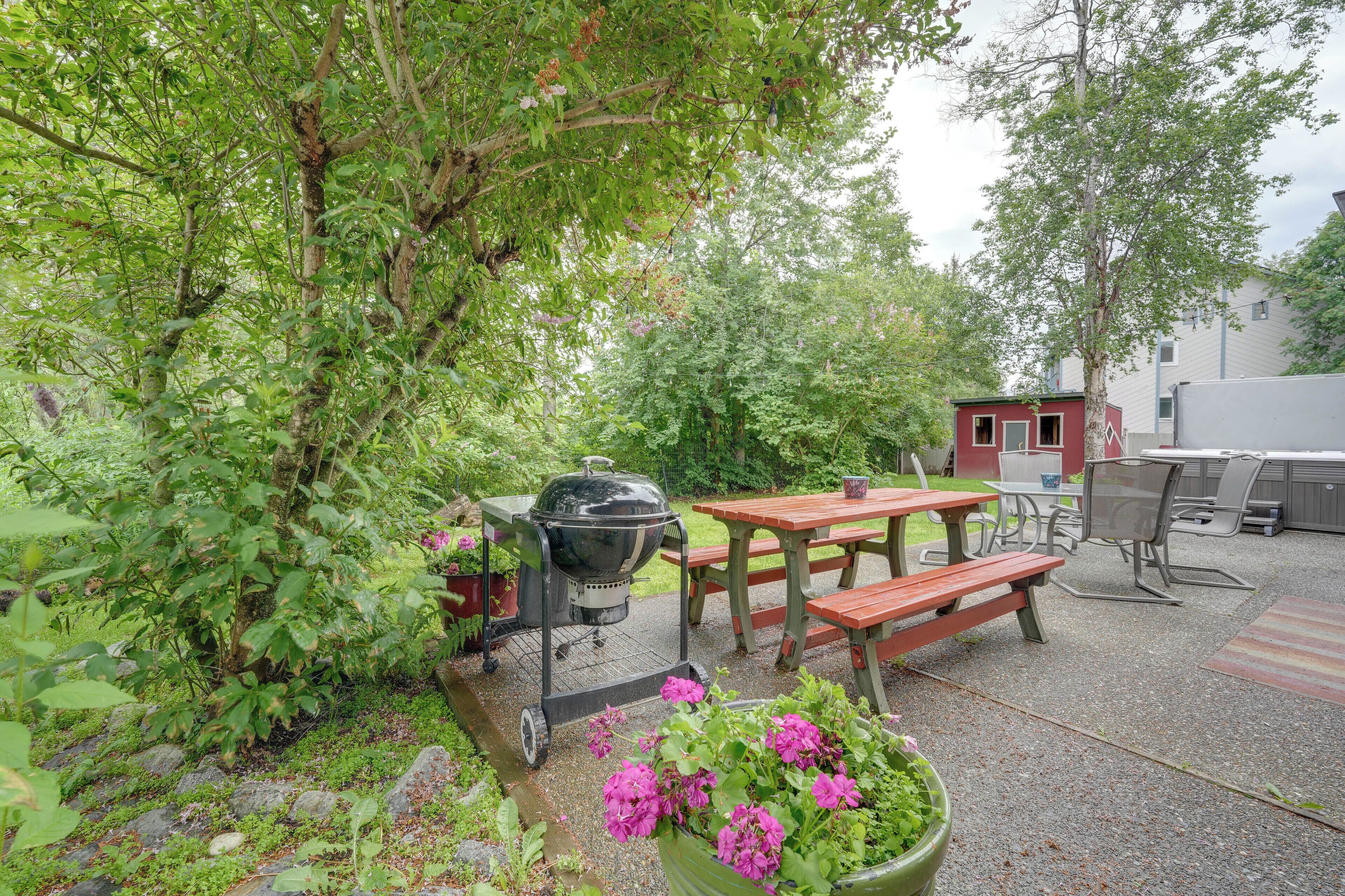 En udendørs terrasse med grill, picnicbord, bænke og plantekasser.