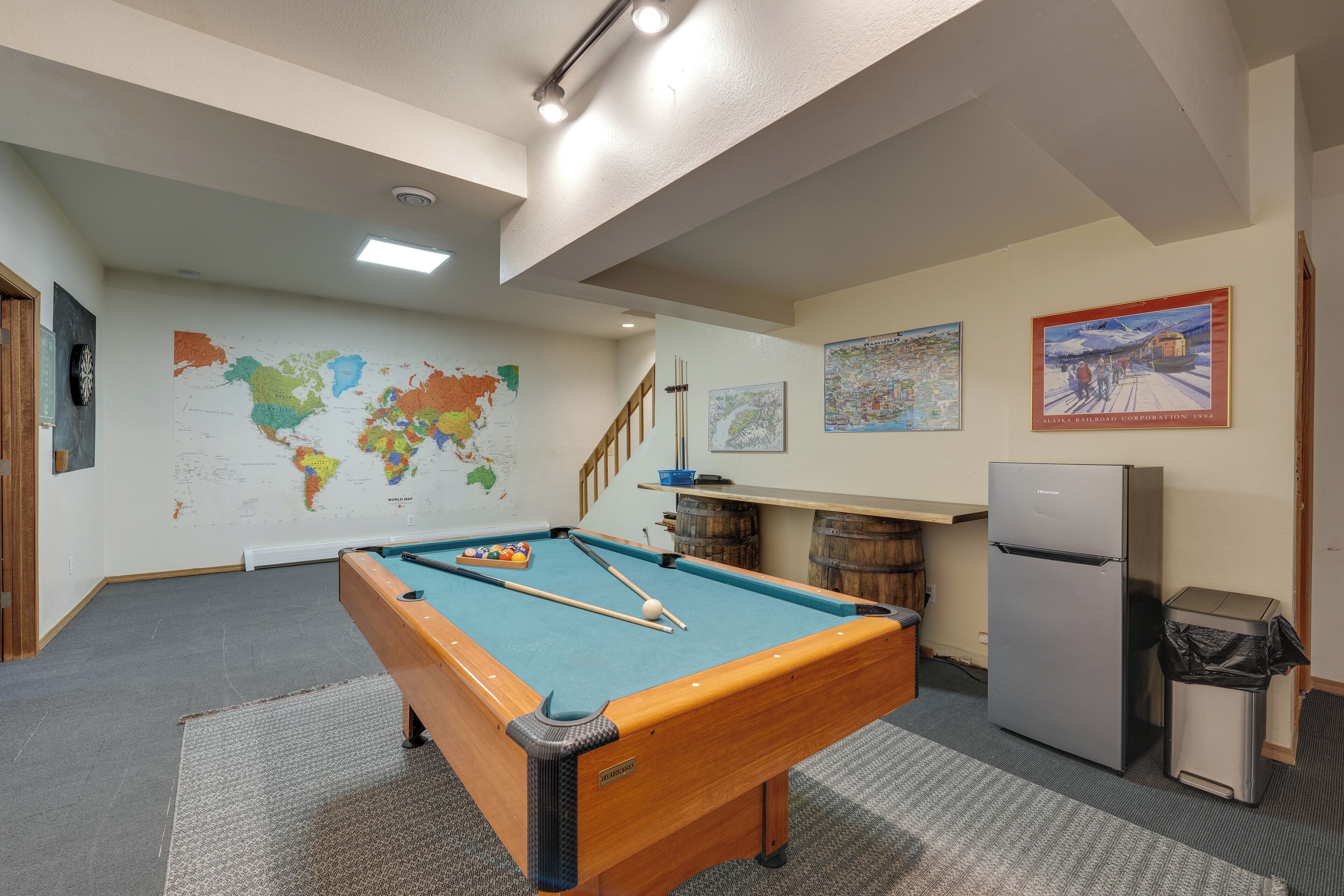 A pool table in a room with a world map, a refrigerator, and a painting on the wall.