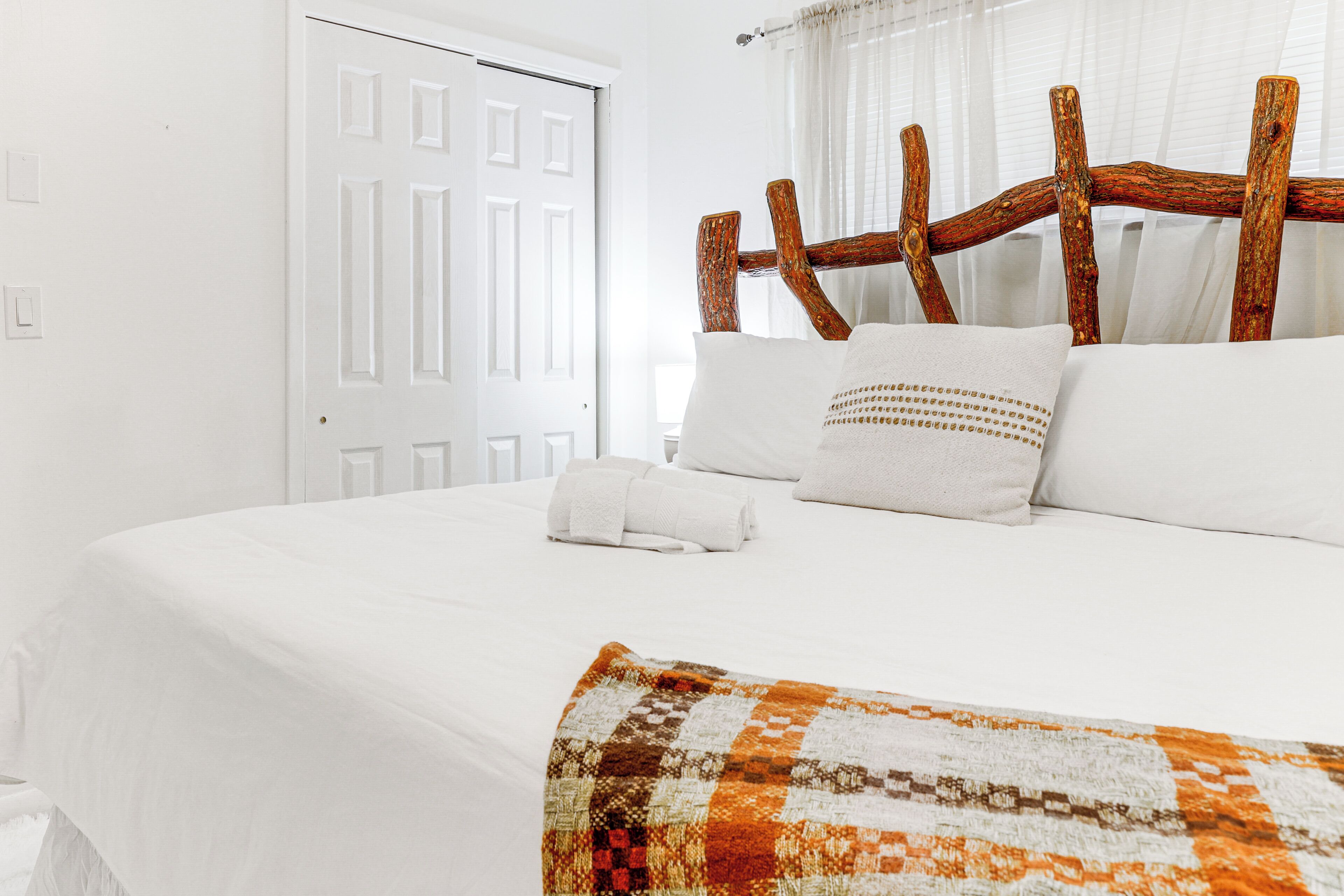 A neatly made bed with white linens, a rustic wooden headboard, and a patterned throw blanket.