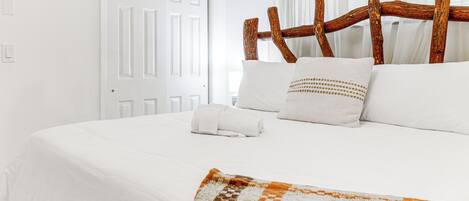 Una cama bien hecha con sábanas blancas, un cabecero de madera rústica y una manta decorativa.