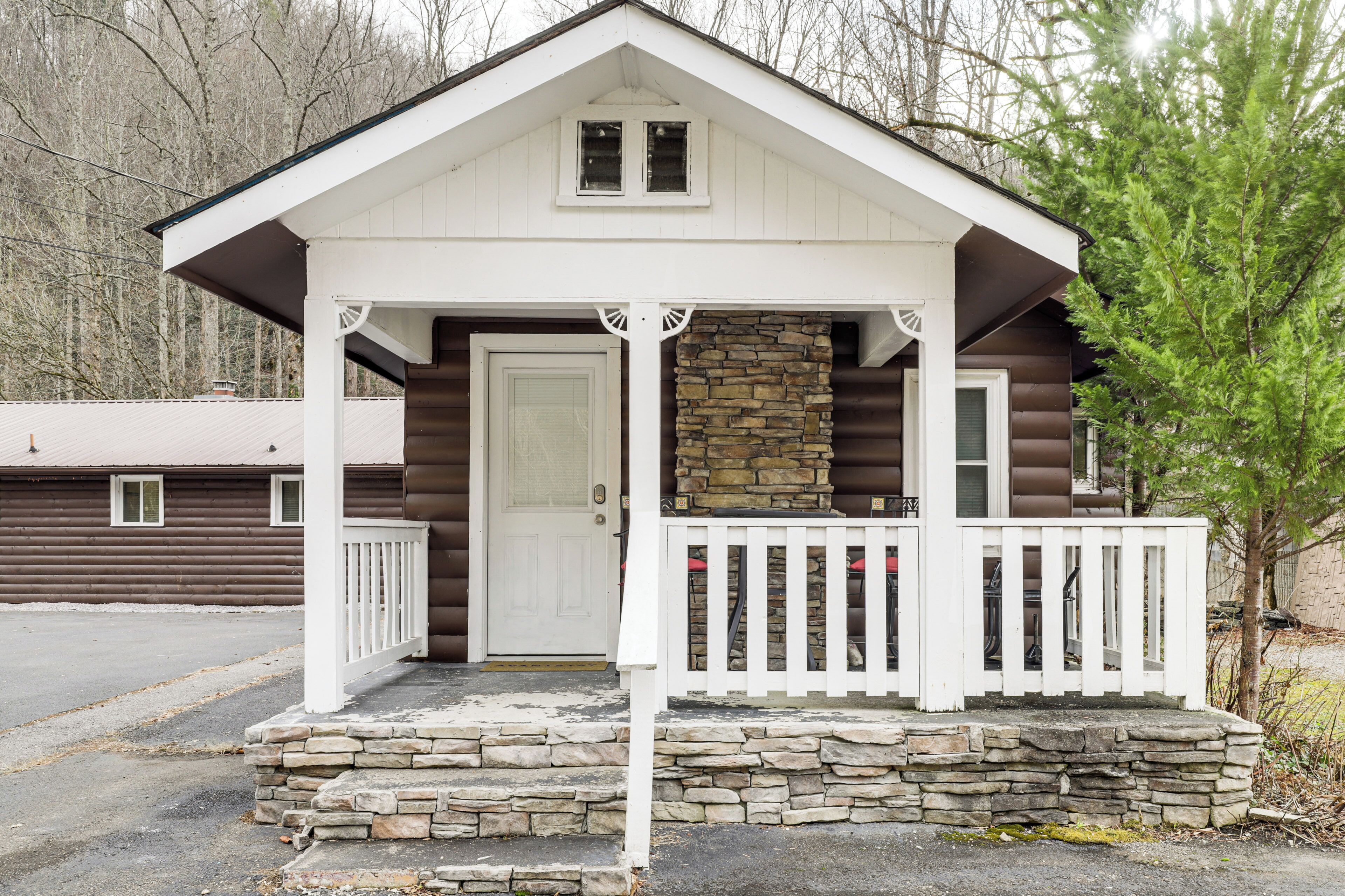 Eine kleine Holzhütte mit steinernen Fundamenten, einer weißen Tür und einer Veranda mit weißen Geländern.