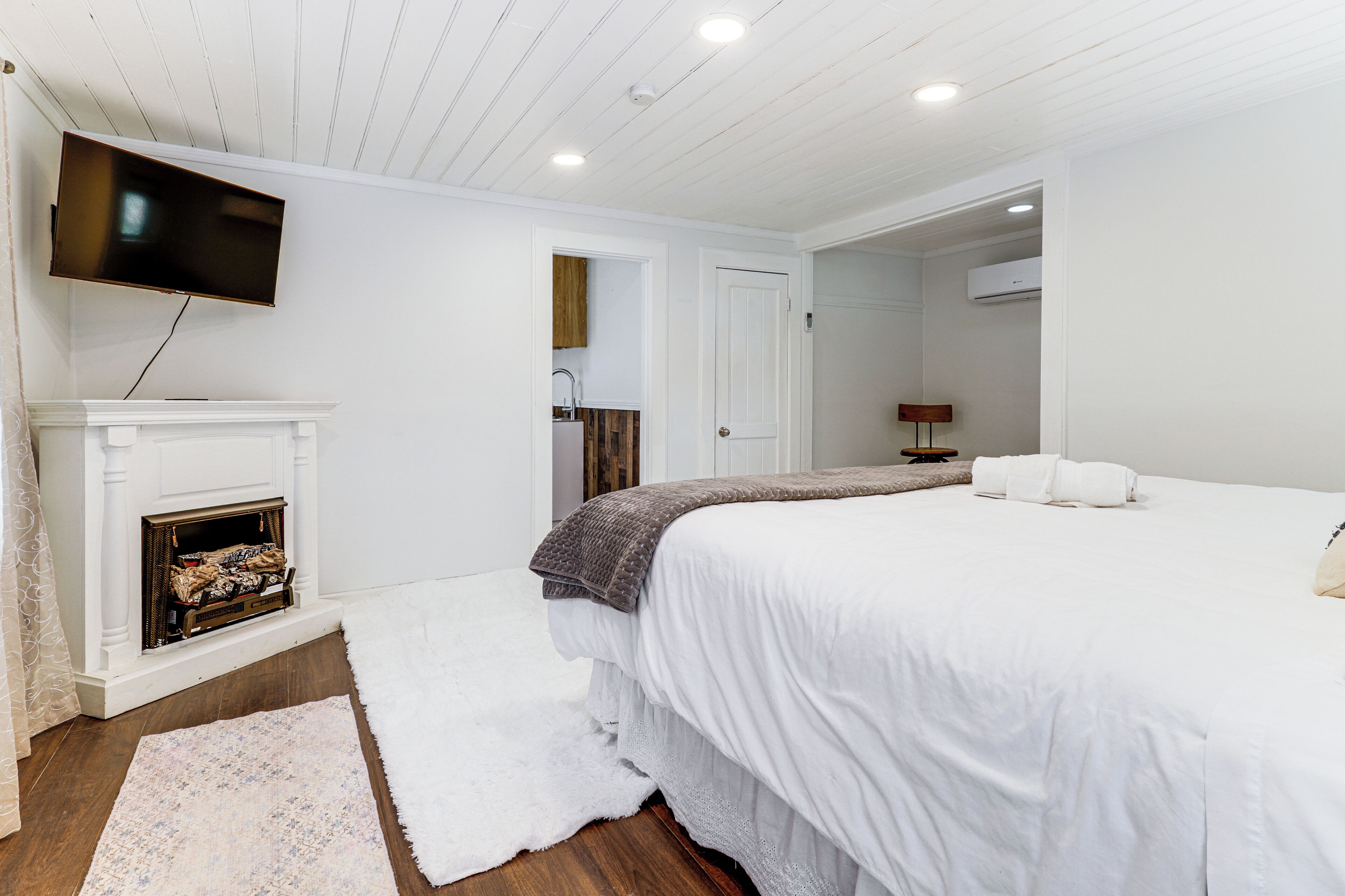 A bedroom with a large bed, a fireplace, a television mounted on the wall, and a door leading to a bathroom.
