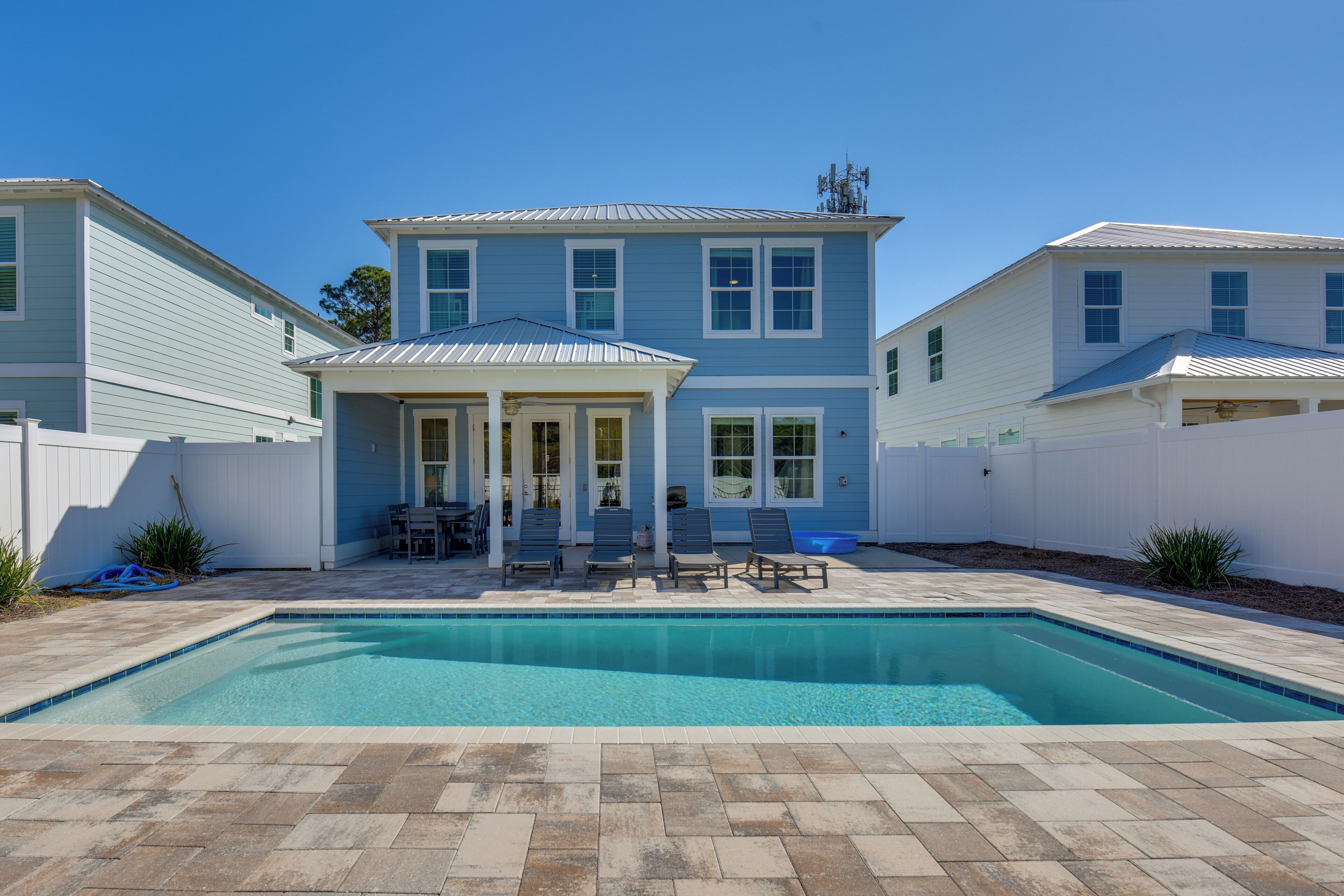 A two-story house with a swimming pool, a covered patio with chairs, and a fenced backyard.