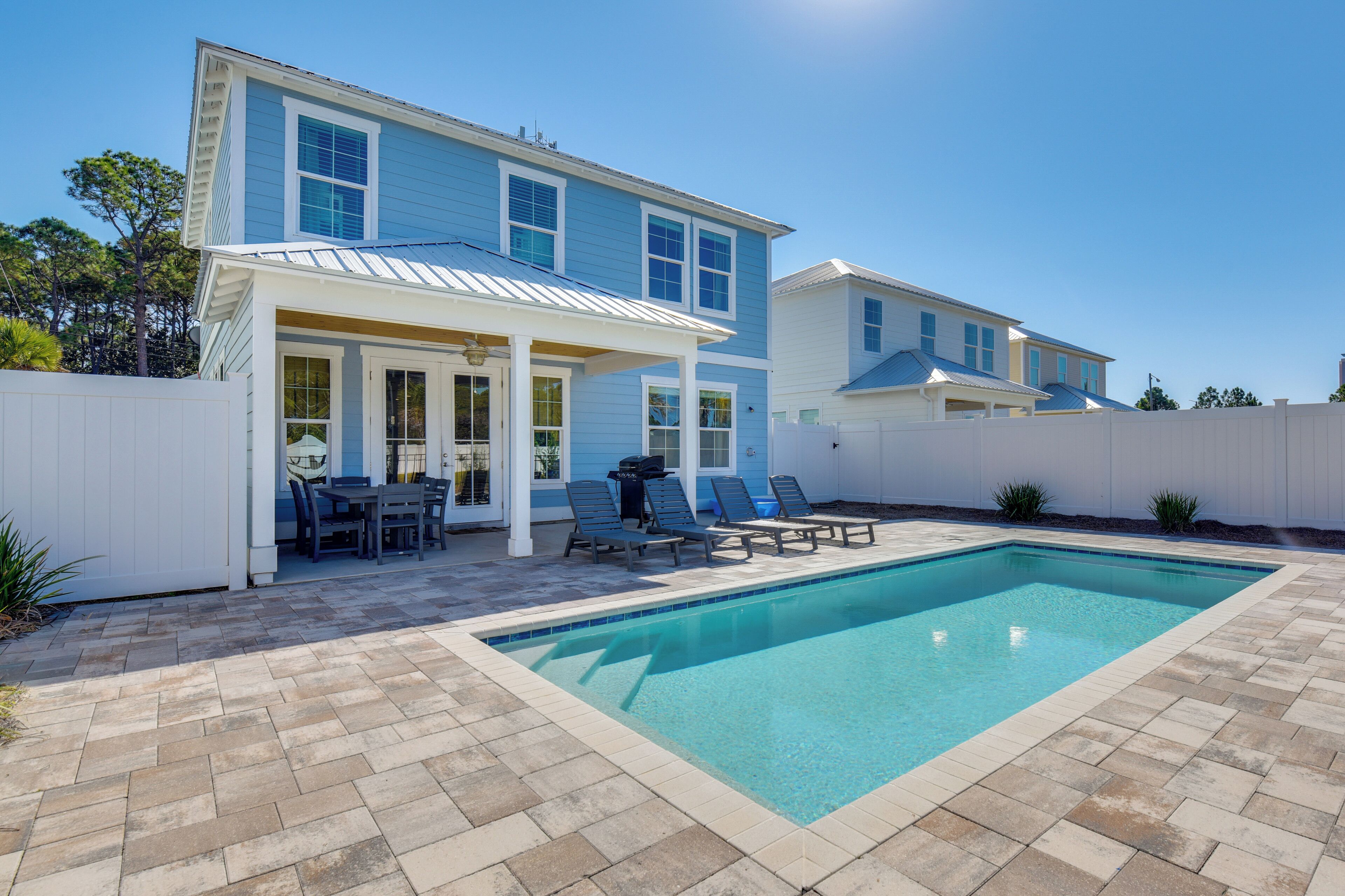 Ein zweistöckiges Haus mit Swimmingpool, einer überdachten Terrasse mit Sitzgelegenheiten und einem eingezäunten Garten.