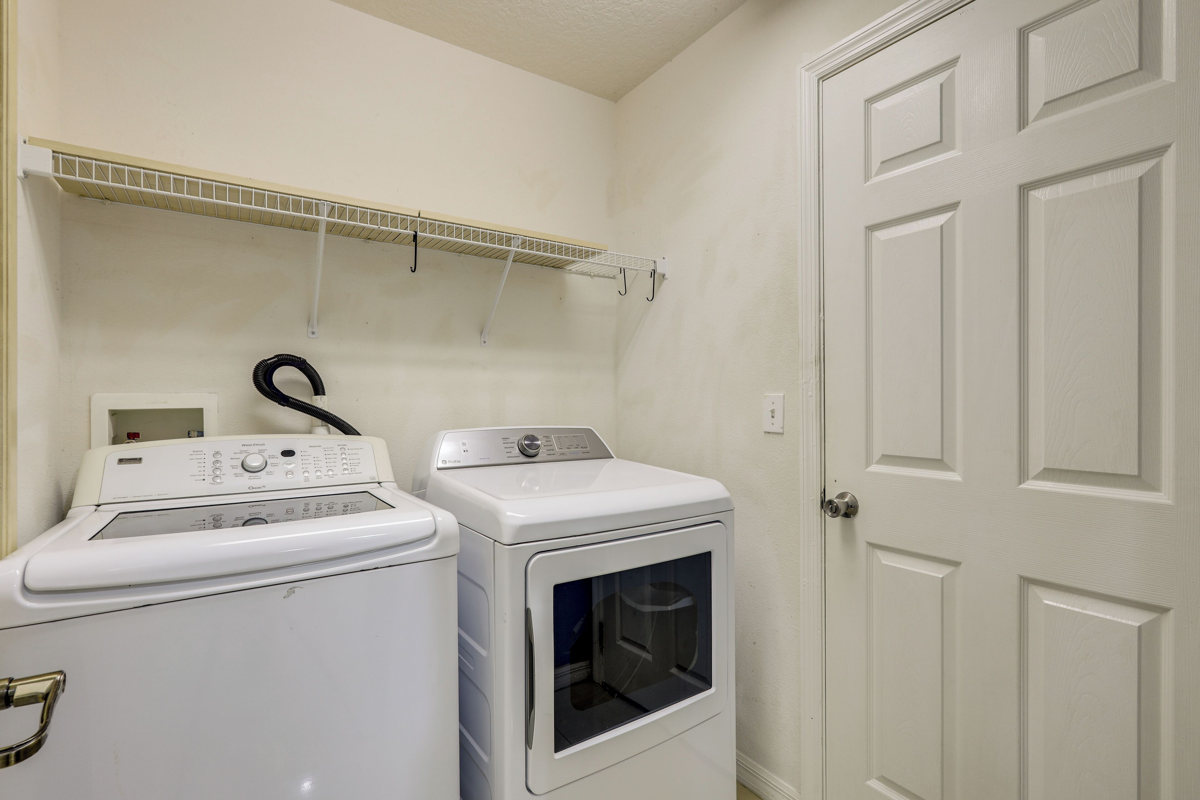 A laundry area with a washing machine and dryer, a metal shelf above, and a white door.