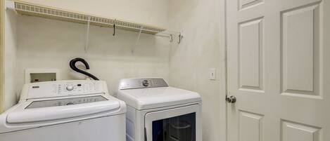 A laundry area with a washing machine and dryer, a metal shelf above, and a white door.