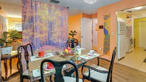 A dining area with a table set for four, chairs, a decorative peacock wall hanging, and a kitchen visible in the background. - Pet-friendly Horse Capital Hub w/ Patio & Yard (Ocala)
