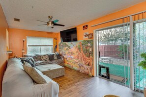 A living room with a sofa, a ceiling fan, a TV, and a mural of animals on the wall. - Pet-friendly Horse Capital Hub w/ Patio & Yard (Ocala)