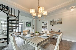 A dining area with a wooden table, white chairs, and a chandelier. - Condo w/ Deck: Waterfront Lake Norman Retreat! (Mooresville)