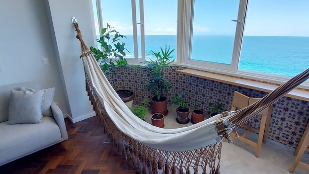 A hammock in a room with a view of the sea, a sofa, and potted plants. - COBAR0108 - Edifício Oceania (Salvador)