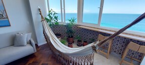 A hammock in a room with a view of the sea, a sofa, and potted plants. - COBAR0108 - Edifício Oceania (Salvador)