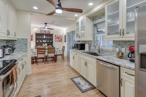 Une cuisine avec des meubles blancs, une table à manger en bois et un ventilateur de plafond.