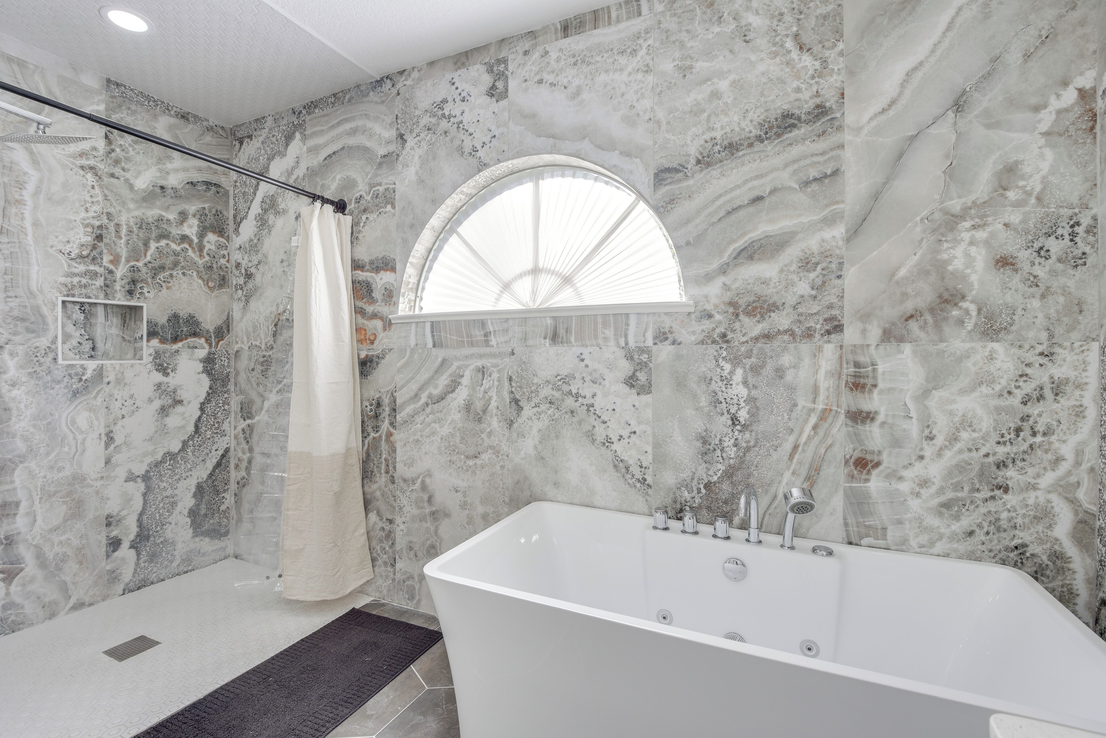 A modern bathroom with a freestanding bathtub, a shower with a curved glass door, and a large arched window.