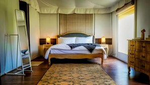 A bedroom with a bed, bedside lamps, a wooden dresser, a standing mirror, and a patterned rug.