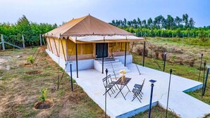 A single-story tent-style structure with a covered patio area, outdoor seating, and a small garden.