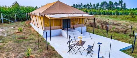 A single-story tent-style structure with a covered patio area, outdoor seating, and a small garden.