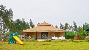 A covered pavilion with a dome roof, surrounded by a grassy area, a playground, and trees.