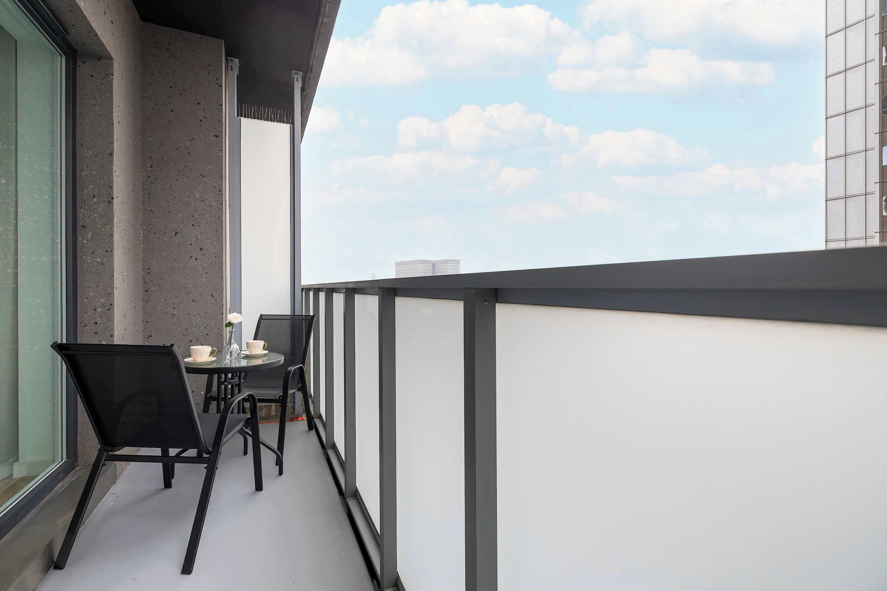 A balcony with a table and chairs, a window, and a view of the sky.