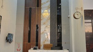 Um lobby moderno com uma receção de mármore, um candelabro e um relógio na parede.