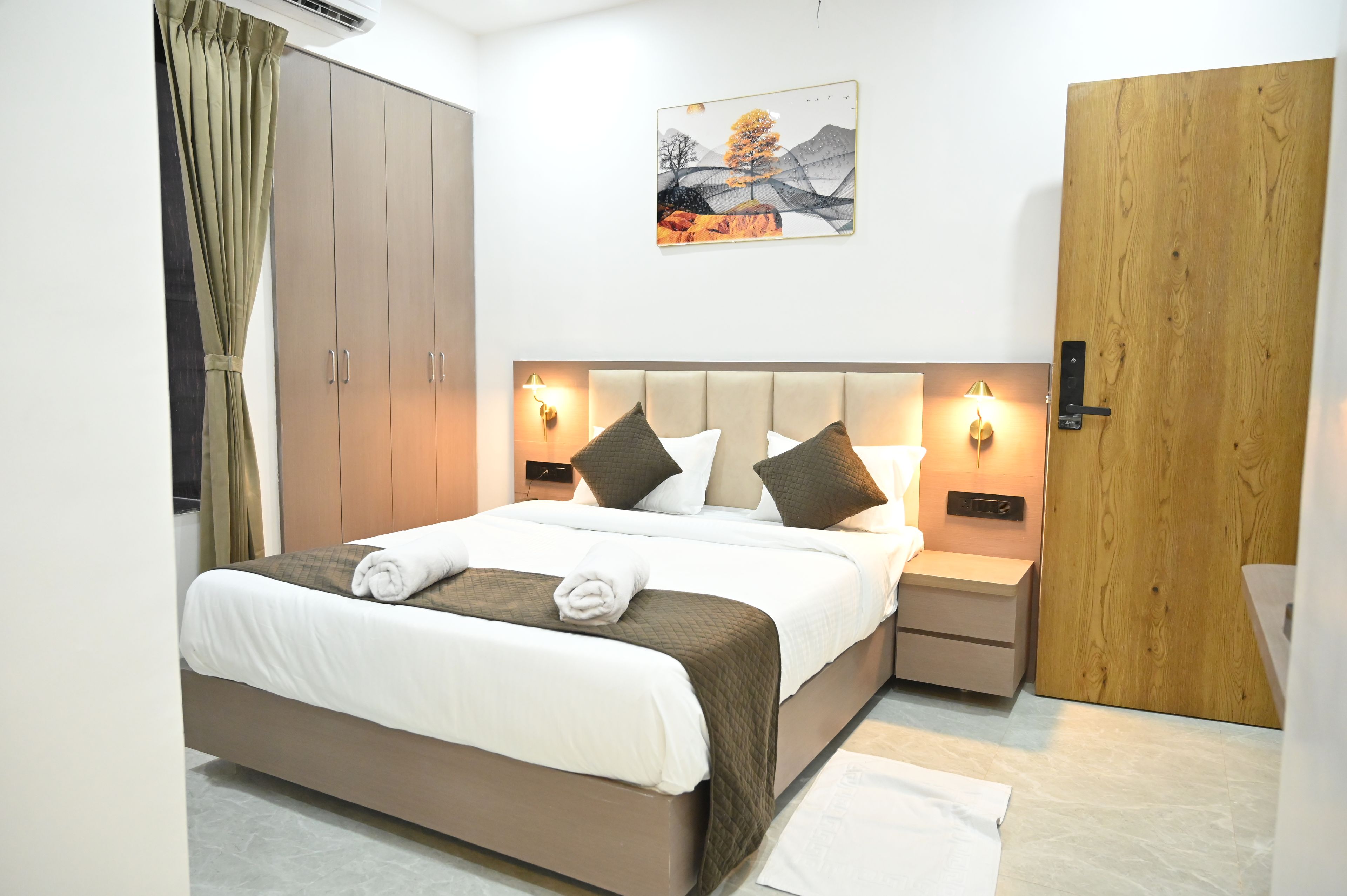 A hotel room with a bed, bedside tables, a wardrobe, a painting, and a door.
