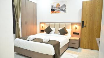 A hotel room with a bed, bedside tables, a wardrobe, a painting, and a door.