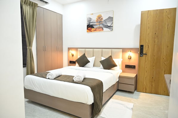 Una habitación de hotel con una cama, mesitas de noche, un armario, un cuadro y una puerta.
