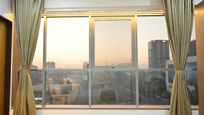 Janela com cortinas, vista de edifícios e reflexo de uma cadeira.