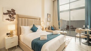 Ein Hotelzimmer mit einem großen Bett, einem Nachttisch mit Lampe, einem Essbereich mit Tisch und Stühlen sowie einem großen Fenster mit Vorhängen.