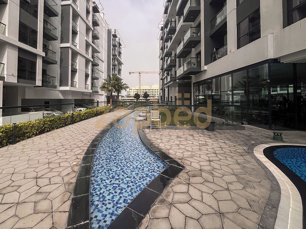 Un moderno complejo de apartamentos con piscina, senderos pavimentados y una grúa de construcción al fondo.