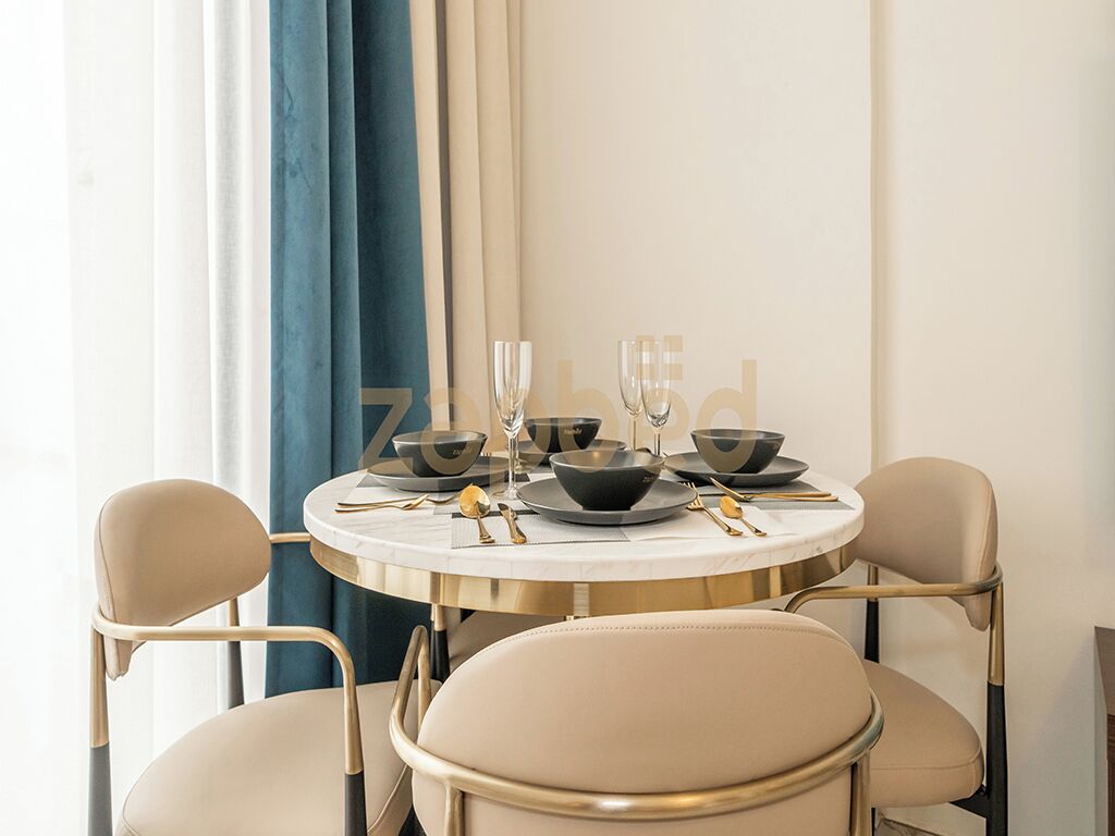 A round dining table with four chairs, set with black bowls, wine glasses, and gold cutlery.