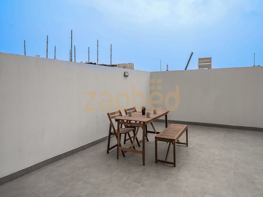 An outdoor patio area with a table and chairs, a bench, and a view of the sky.