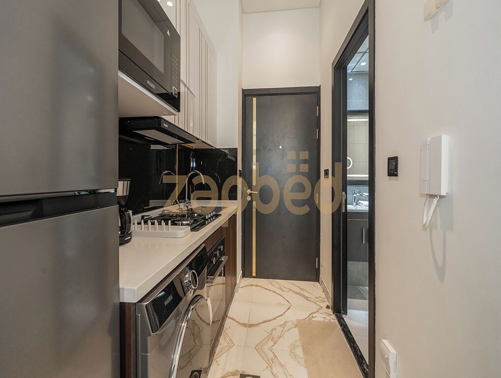 A modern kitchen with stainless steel appliances, a marble backsplash, and a sleek black door.
