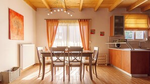 A dining area with a wooden table and chairs, a kitchen with wooden cabinets and a window, and a ceiling with exposed beams.