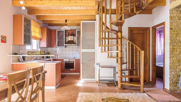 A spacious kitchen with wooden cabinets, a dining area with chairs, a central island, and a spiral staircase leading to an upper level.