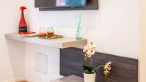 A modern room with a flat-screen TV mounted on the wall, a small white table with a potted plant, and a wooden floor. - GuestHost - Spacious room with balcony that can accommodate up to 4 people, located in a convenient and central position, in a building with concierge. The accommodation is located just 10 minutes walk from the historic center, in an area equipped with e (Bari)