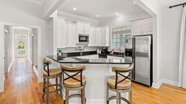 A spacious kitchen with white cabinets, a stainless steel refrigerator, and a large island with bar stools. - Private House w/Private Pool, 0.3 miles from beach + Free Attraction Tickets! (North Myrtle Beach)