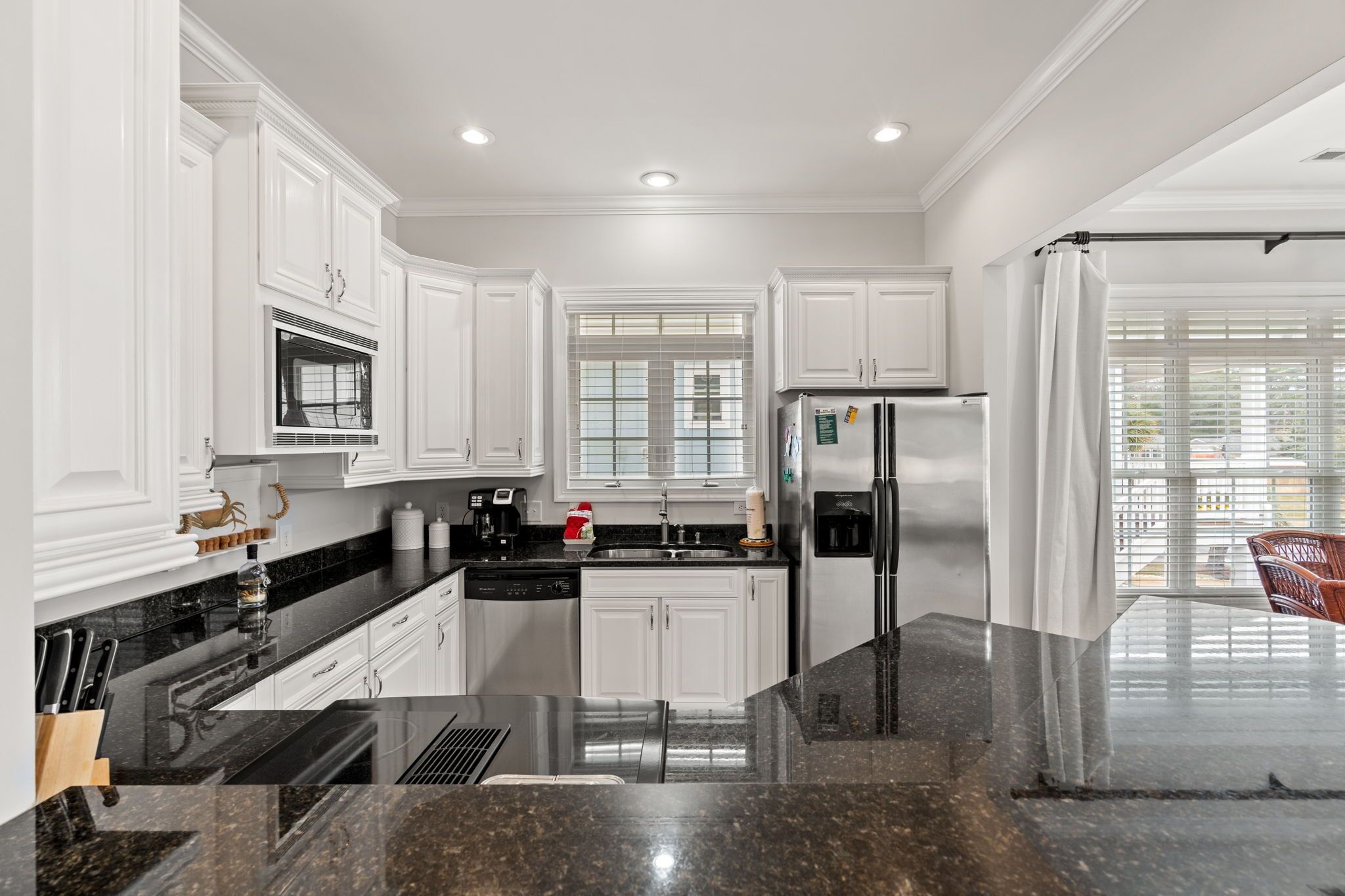 A modern kitchen with white cabinetry, a stainless steel refrigerator, and a granite countertop.