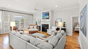 A spacious living room with a fireplace, a ceiling fan, and a large window with blinds. - Private House w/Private Pool, 0.3 miles from beach + Free Attraction Tickets! (North Myrtle Beach)