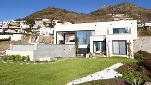 Une maison moderne à deux étages, dotée d’un toit plat, de grandes fenêtres et d’une pelouse bien entretenue.