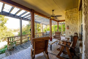 Eine überdachte Terrasse mit Holzmöbeln, einem Deckenventilator und einer Steinwand.
