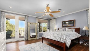 Ein Schlafzimmer mit einem großen Bett, einem Deckenventilator, einem Fenster mit Vorhängen, einem Schminktisch und einem Nachttisch mit Lampe.