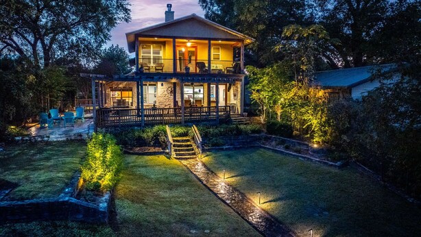 Ein zweistöckiges Haus mit überdachter Veranda, einem gut beleuchteten Garten und einer Treppe, die zum Eingang führt.