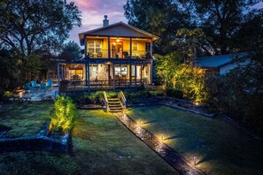 Een tweelaags huis met een overdekte veranda, een goed verlichte voortuin en een trap naar de ingang.
