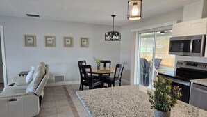 Een moderne keuken met een granieten werkblad, een eethoek met een ronde tafel en stoelen, en een bank in de woonkamer.