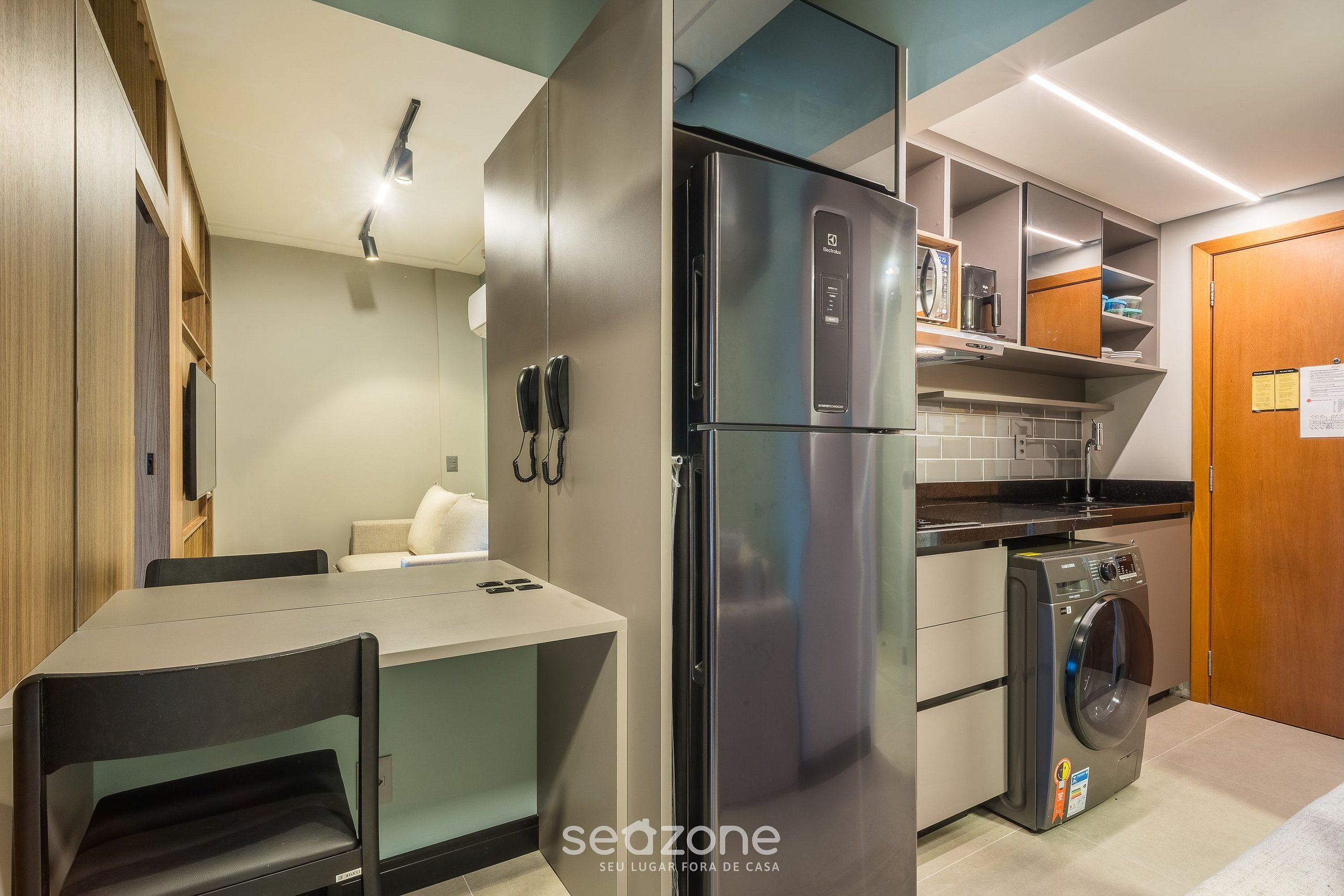 A compact kitchen with a refrigerator, washing machine, and a small dining area.