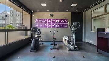 A gym with exercise equipment, a wall clock, and a view of buildings outside.
