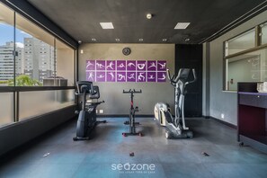 Une salle de sport équipée de matériel d’exercice, avec une horloge murale et une vue sur les bâtiments environnants.