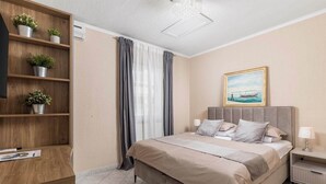 Een slaapkamer met een bed, nachtkastjes, een boekenplank en een schilderij aan de muur.