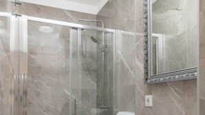 Een moderne badkamer met een douchecabine van glas, een witte wastafel en een houten opbergmeubel.