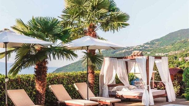 Een zwembadterras met ligbedden, parasols en een hemelbed.